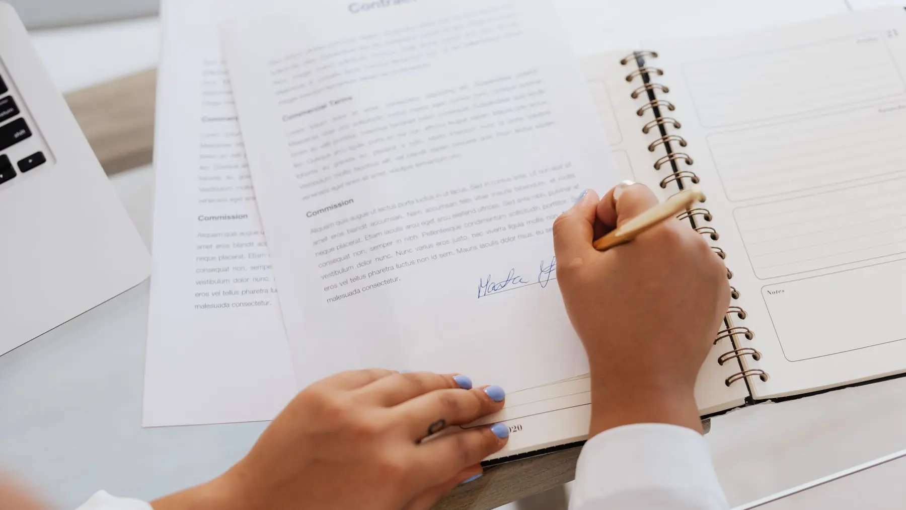 Mano tomando notas en un cuaderno junto a un contrato, sobre la mesa
