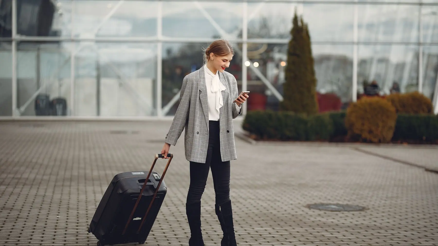 Viajera consultando el móvil mientras arrastra su maleta