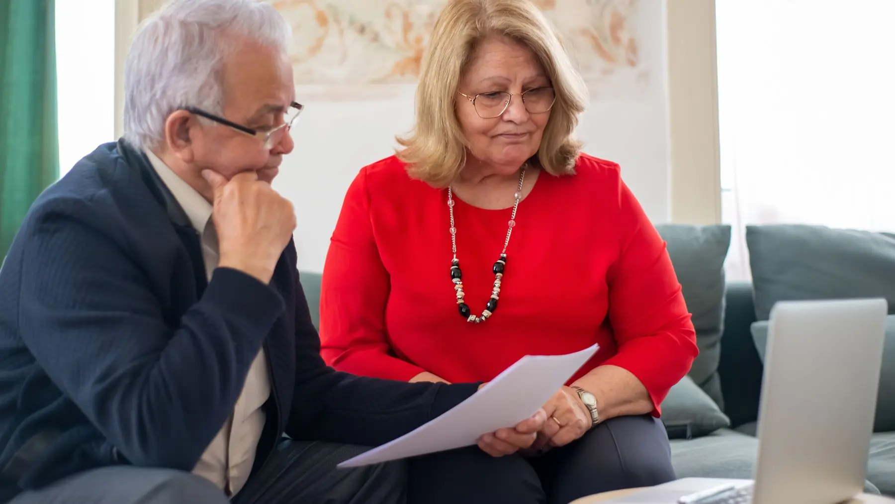 Pareja mayor revisando documentación sentados en el sofá de casa